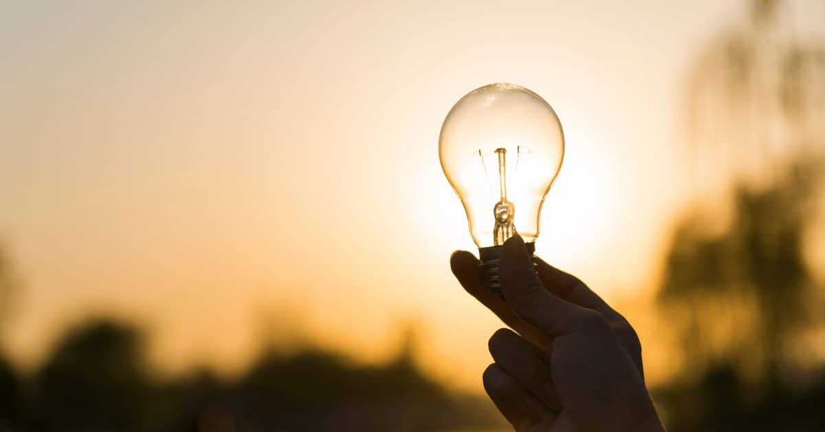 Hand holding a light bulb against a sunset sky