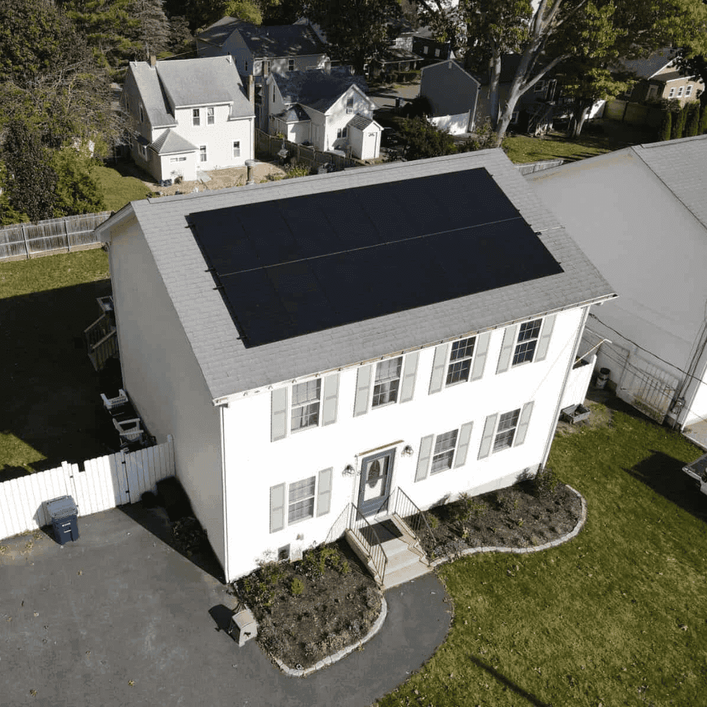 Aerial view of a New England home with fresh solar panels installed across the roof, showcasing a clean, efficient system designed to maximize sunlight and energy savings.