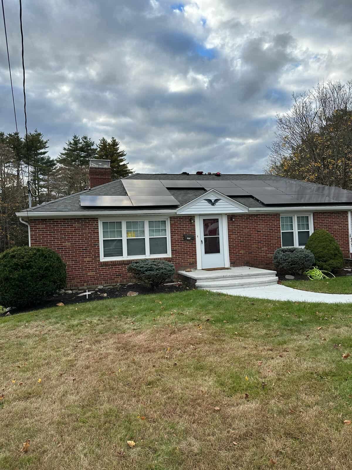 Front view of a brick single-story home with rooftop solar panels installed, showcasing residential solar installation, clean energy generation, and long-term solar savings for New England homeowners.