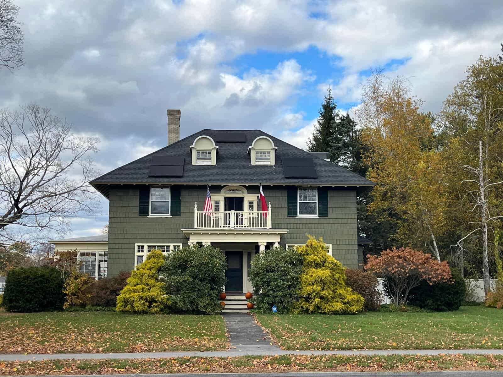 Two-story historic-style home with dark asphalt shingles and black solar panels installed on the roof, showing a residential solar energy system designed to reduce electric bills and increase long-term solar savings for homeowners.