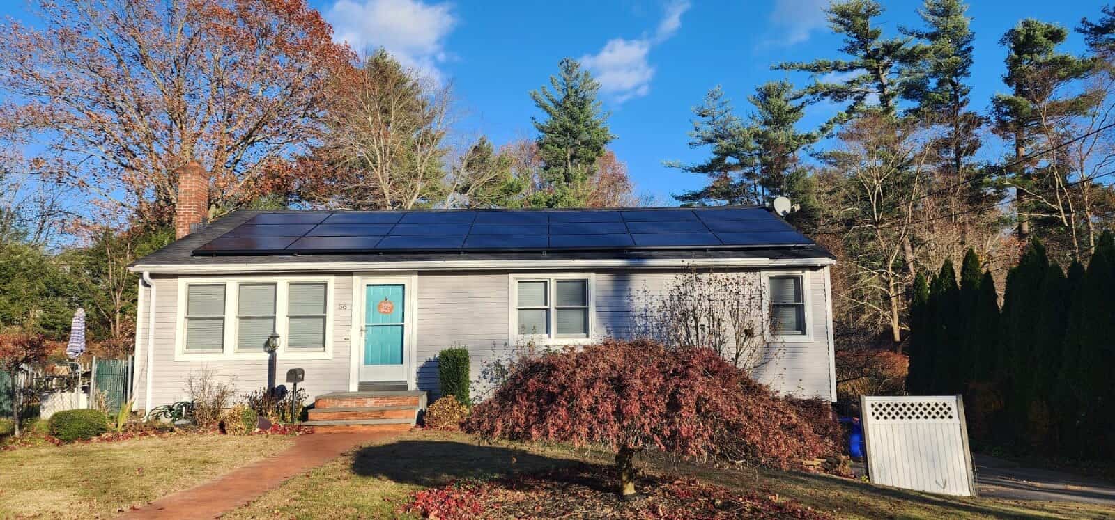 Single-story home with a bright blue front door, featuring a full rooftop solar panel array covering nearly the entire front roofline.