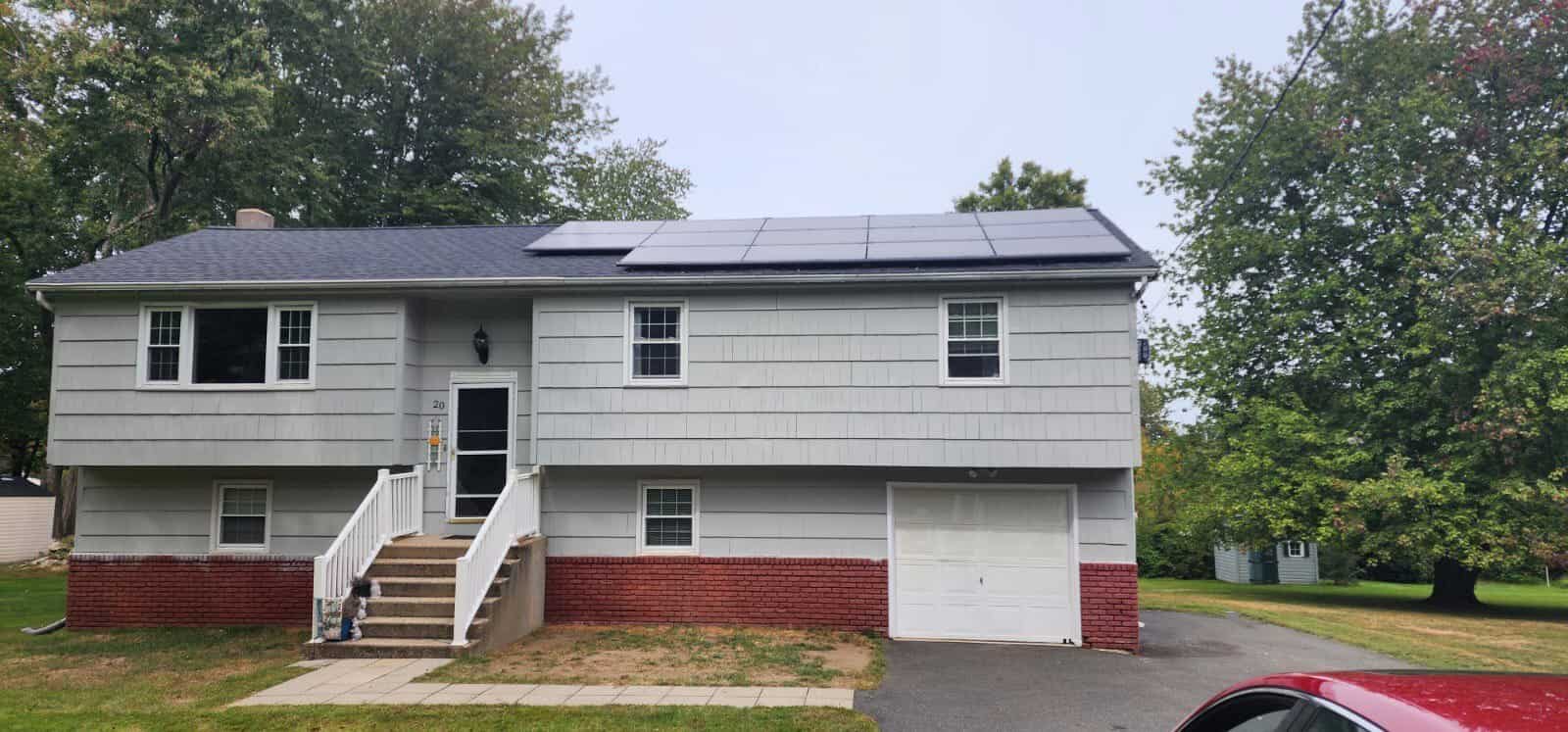 Gray split-level home with red brick foundation, featuring a row of sleek black solar panels installed across the upper roofline.