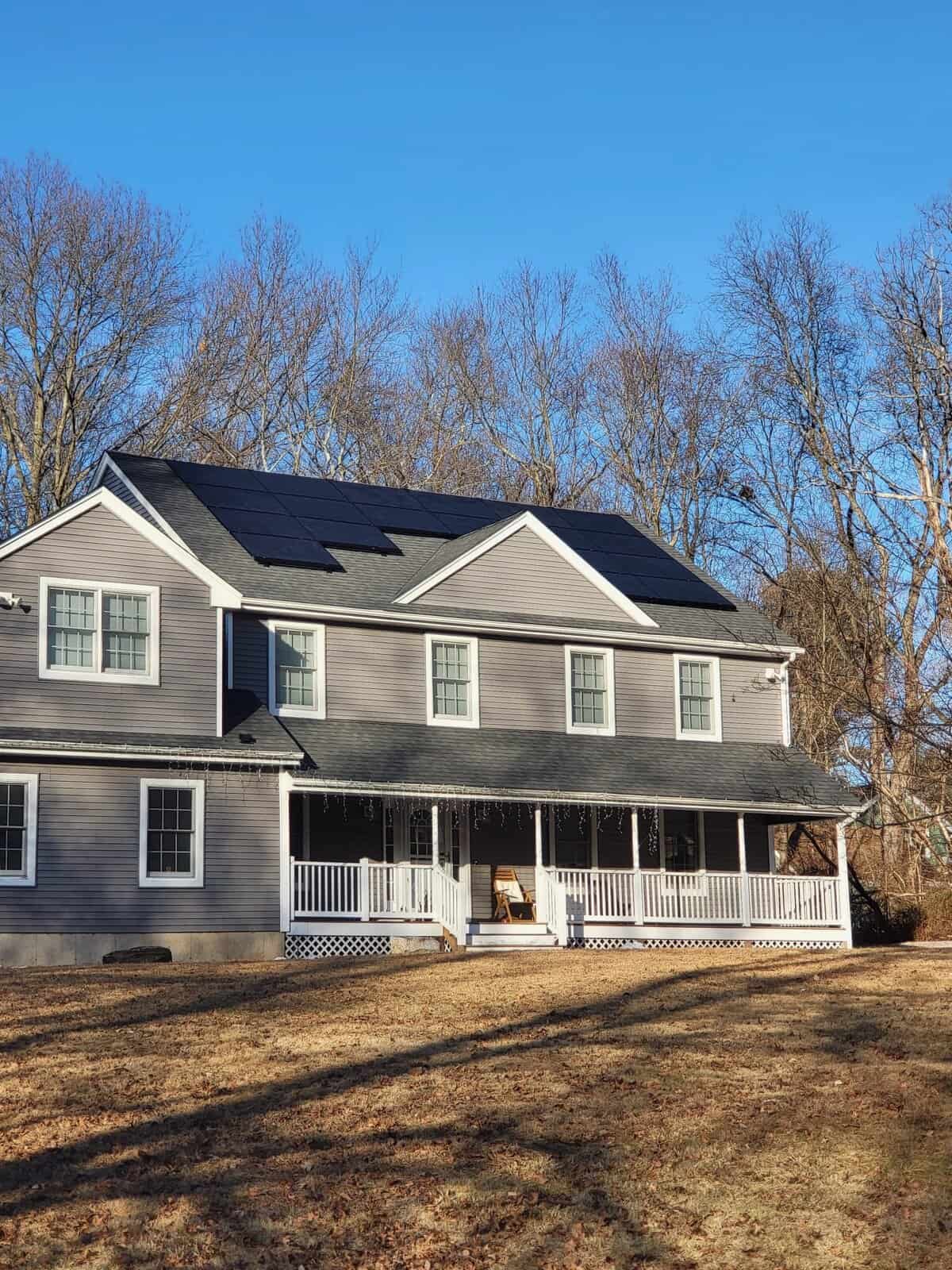 Two-story gray house with front porch and black solar panels across the roof, providing renewable energy and long-term savings.
