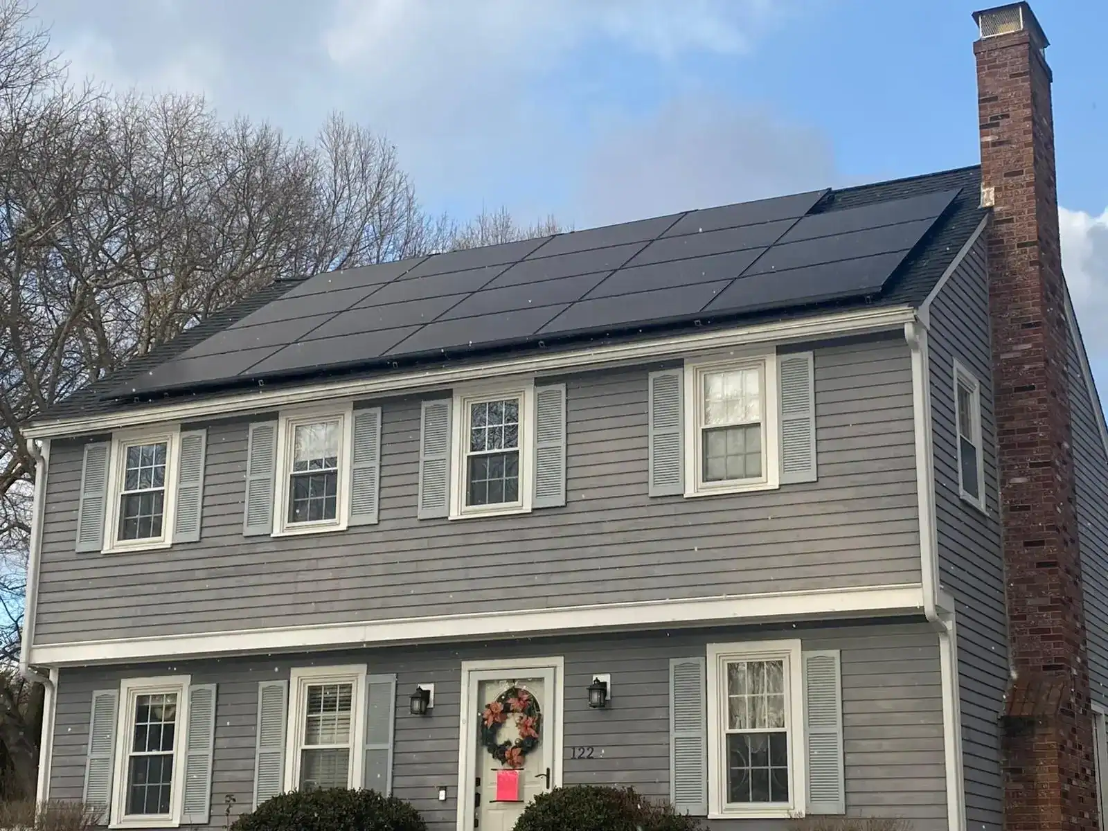 Gray two-story home with black solar panels installed across the roof, lowering energy costs with renewable power.