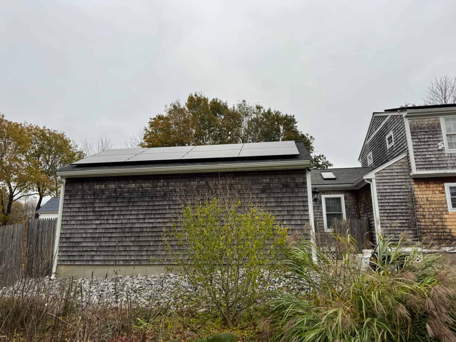 Detached shingle-style garage with roof-mounted solar panels, part of a residential solar installation designed to increase energy efficiency, reduce electricity costs, and deliver long-term solar savings for a New England home.
