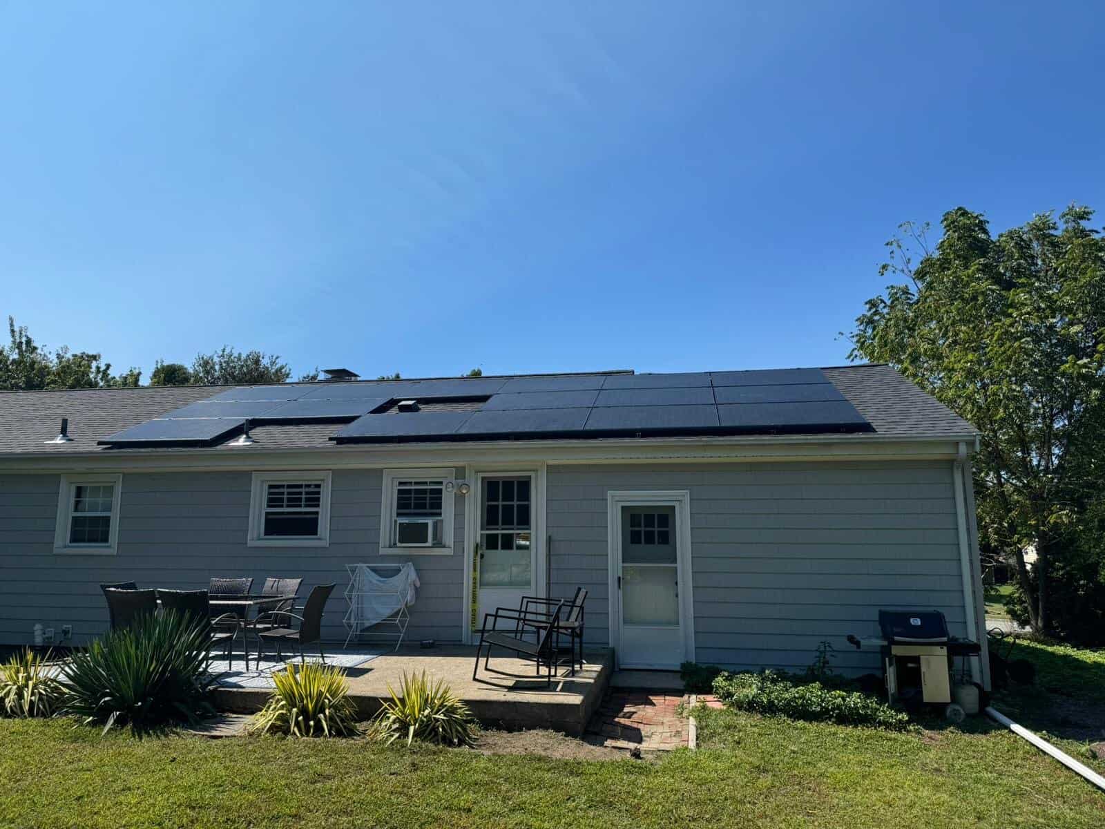 Gray single-story home with a wide back patio, topped by a full array of sleek black solar panels spanning the roofline.