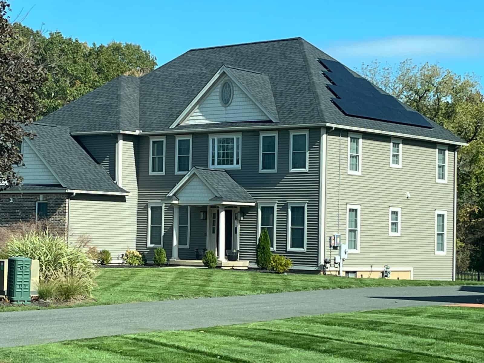 Two-story New England home with black rooftop solar panels installed on an asphalt shingle roof, showcasing residential solar installation, clean energy upgrades, and long-term solar savings for homeowners with a well-maintained lawn and modern exterior.