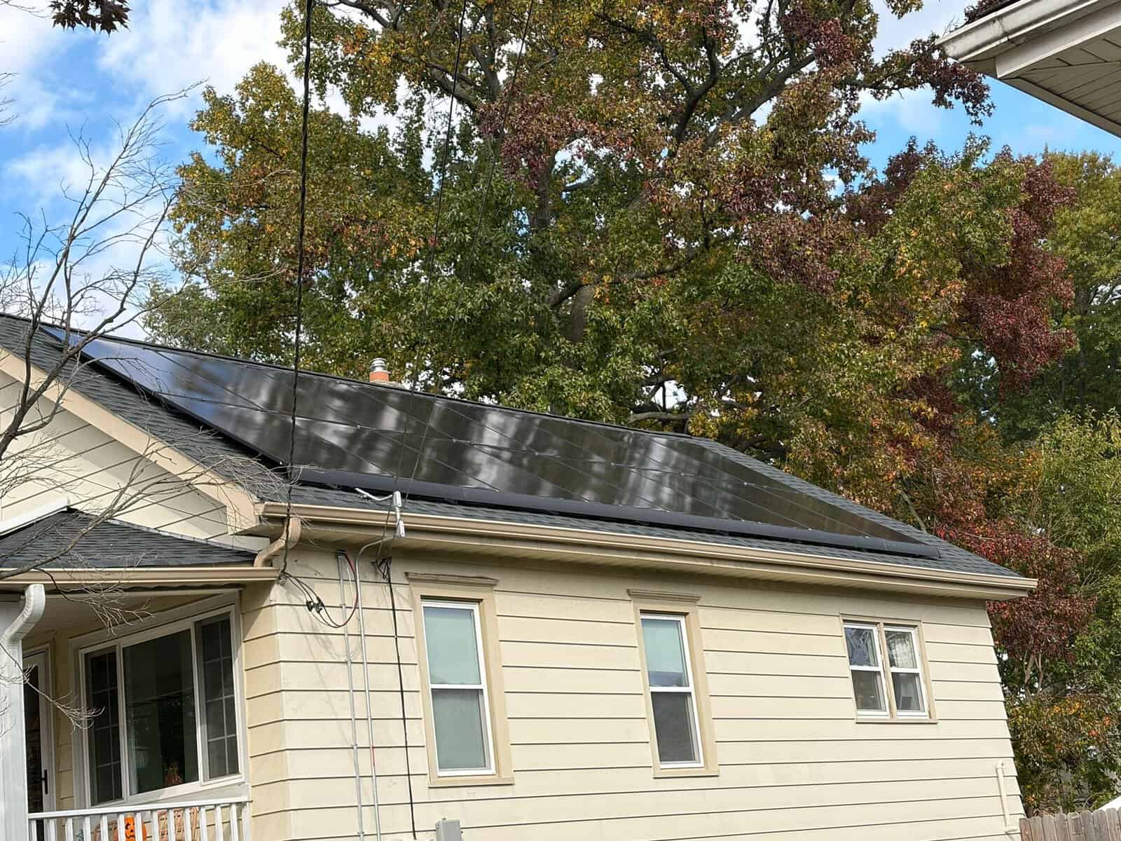 A beige-sided home with a low-profile black solar array installed along the rear roof slope, framed by mature autumn trees.