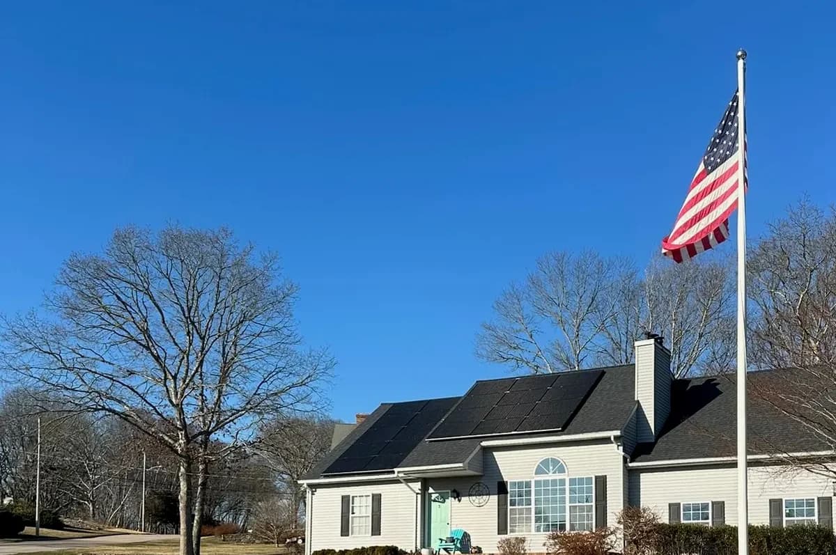 Solar-powered home with black solar panels installed on the roof, situated in a well-maintained yard with green grass, surrounded by leafless trees, under a clear blue sky, demonstrating renewable energy and eco-friendly living.