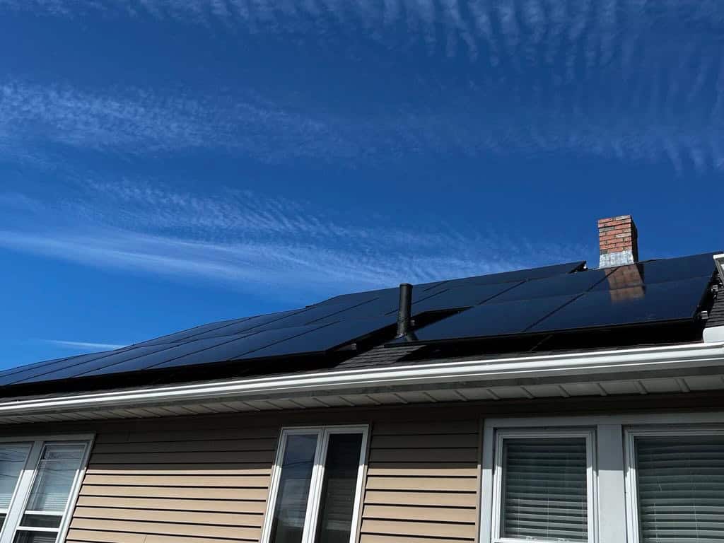 Photovoltaic solar panels installed on a residential roof under a clear blue sky with wispy clouds.