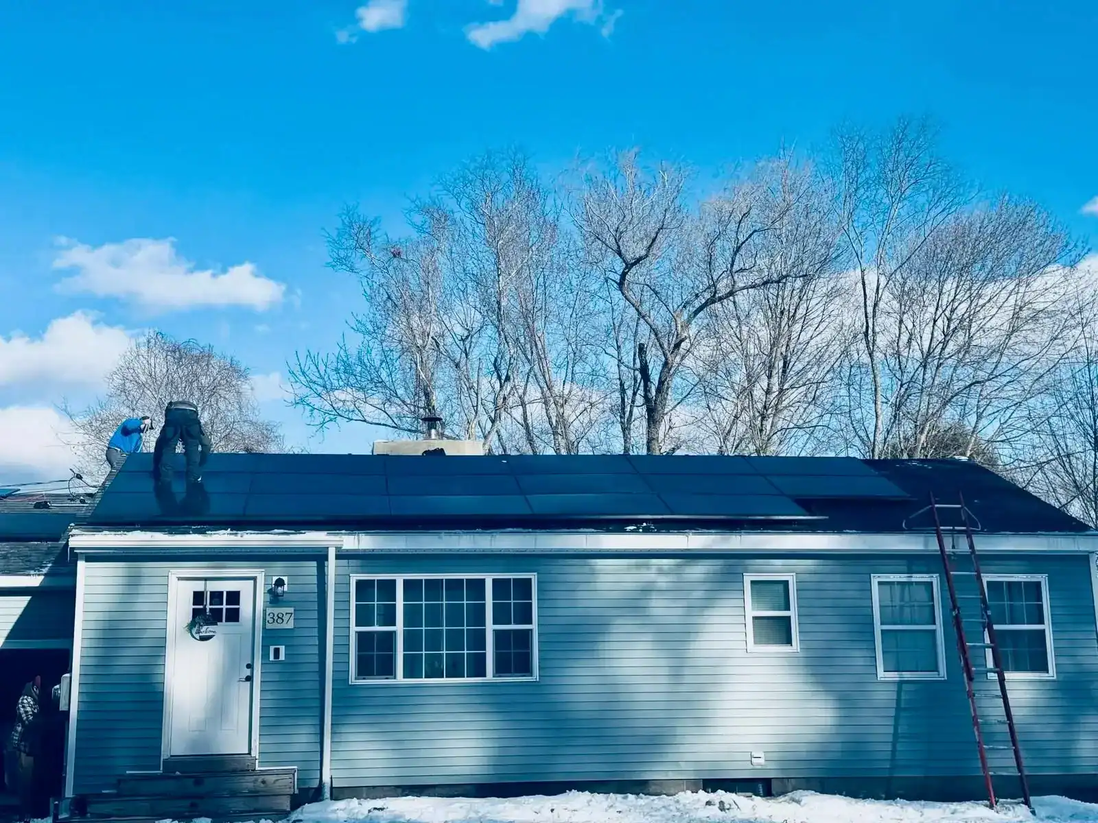 Solar panel installation on a residential roof with workers, blue sky, and leafless trees in winter, demonstrating home solar energy system setup for renewable power generation.