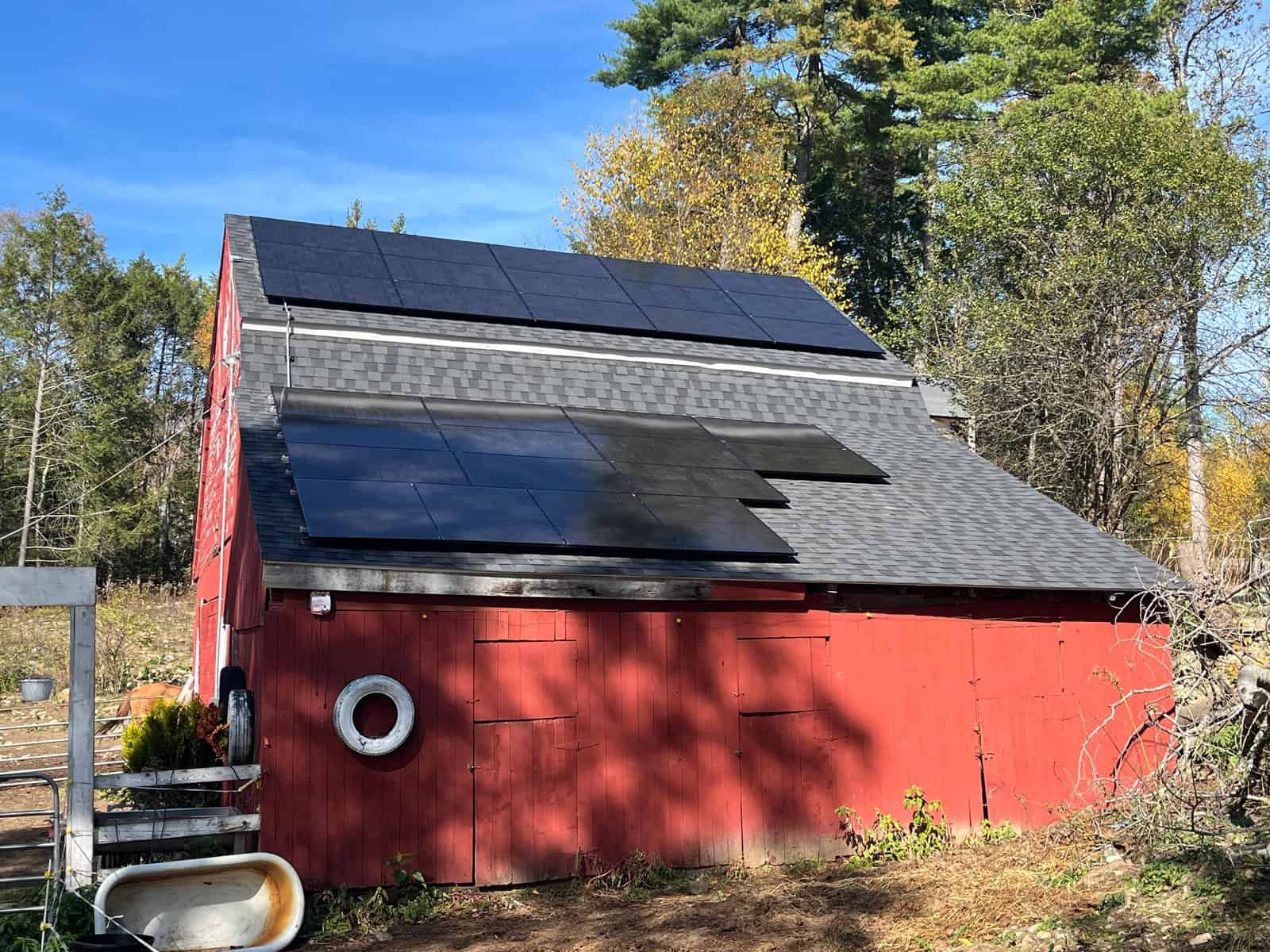 Red barn with rooftop solar panels installed on an asphalt shingle roof, showcasing agricultural solar installation, renewable energy for rural properties, and long-term solar savings through clean energy upgrades.