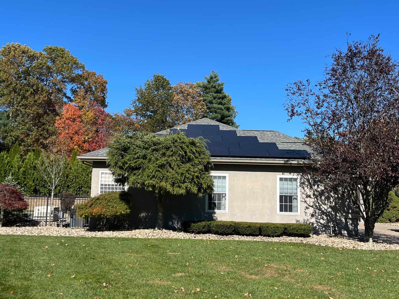Single-story New England home with a ground-facing roofline featuring black solar panels, highlighting residential solar installation, clean energy solutions, and long-term solar savings, set against fall foliage and a clear blue sky.