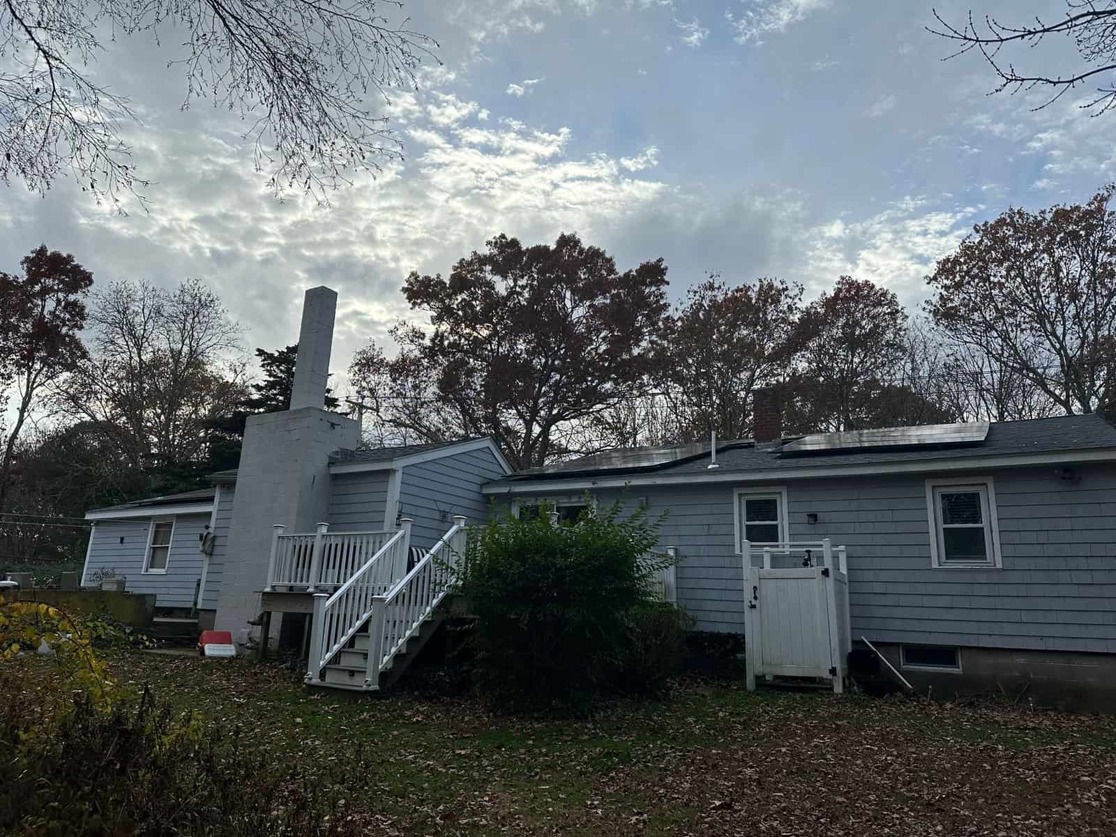 Single-story light gray home with white trim and a tall rectangular chimney, featuring rooftop solar panels installed on the rear slope of the roof.