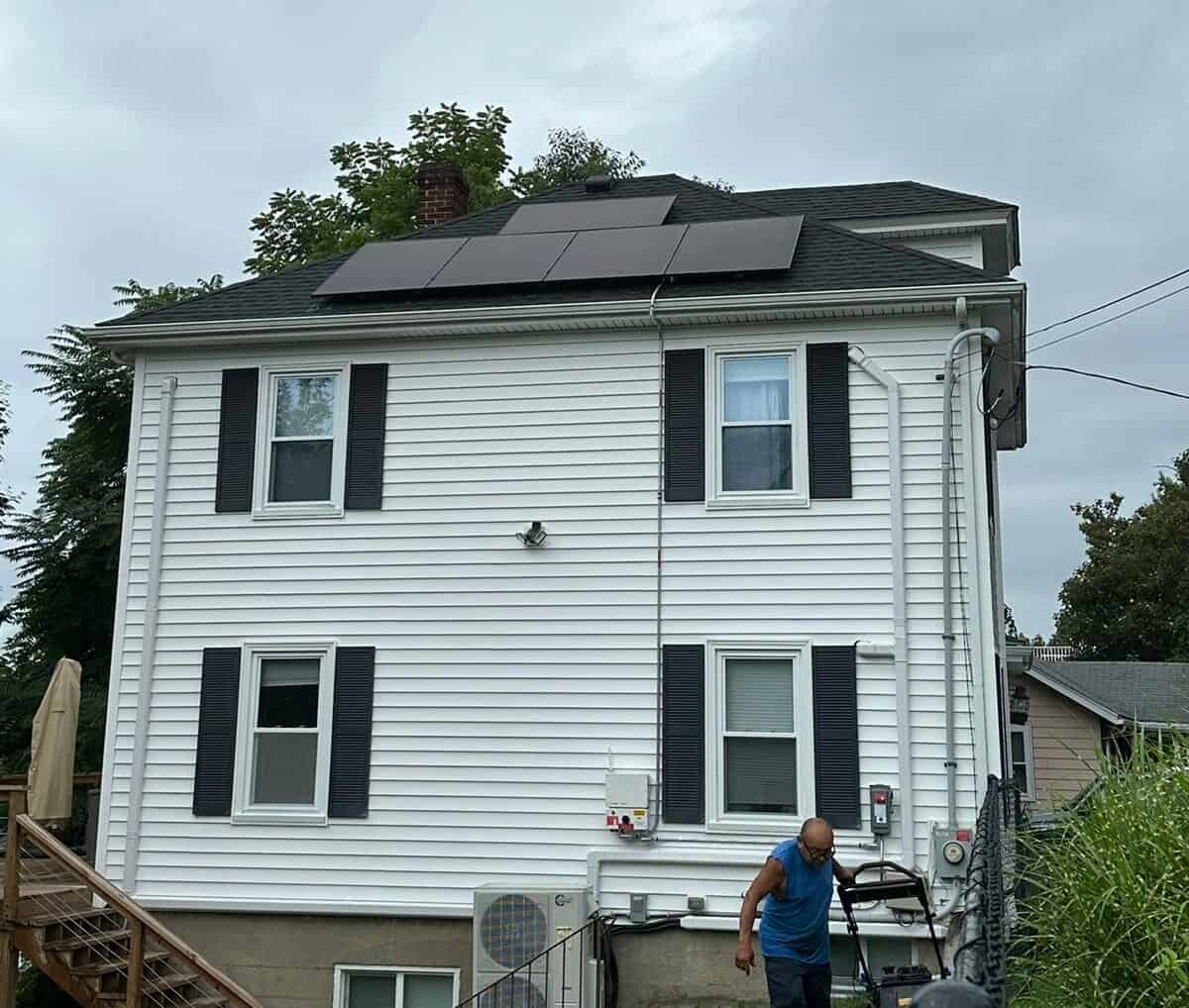 Solar panels installed on the roof of a white multi-story house, with a man walking below, showcasing residential solar energy solutions for sustainable power generation, eco-friendly and cost-effective.