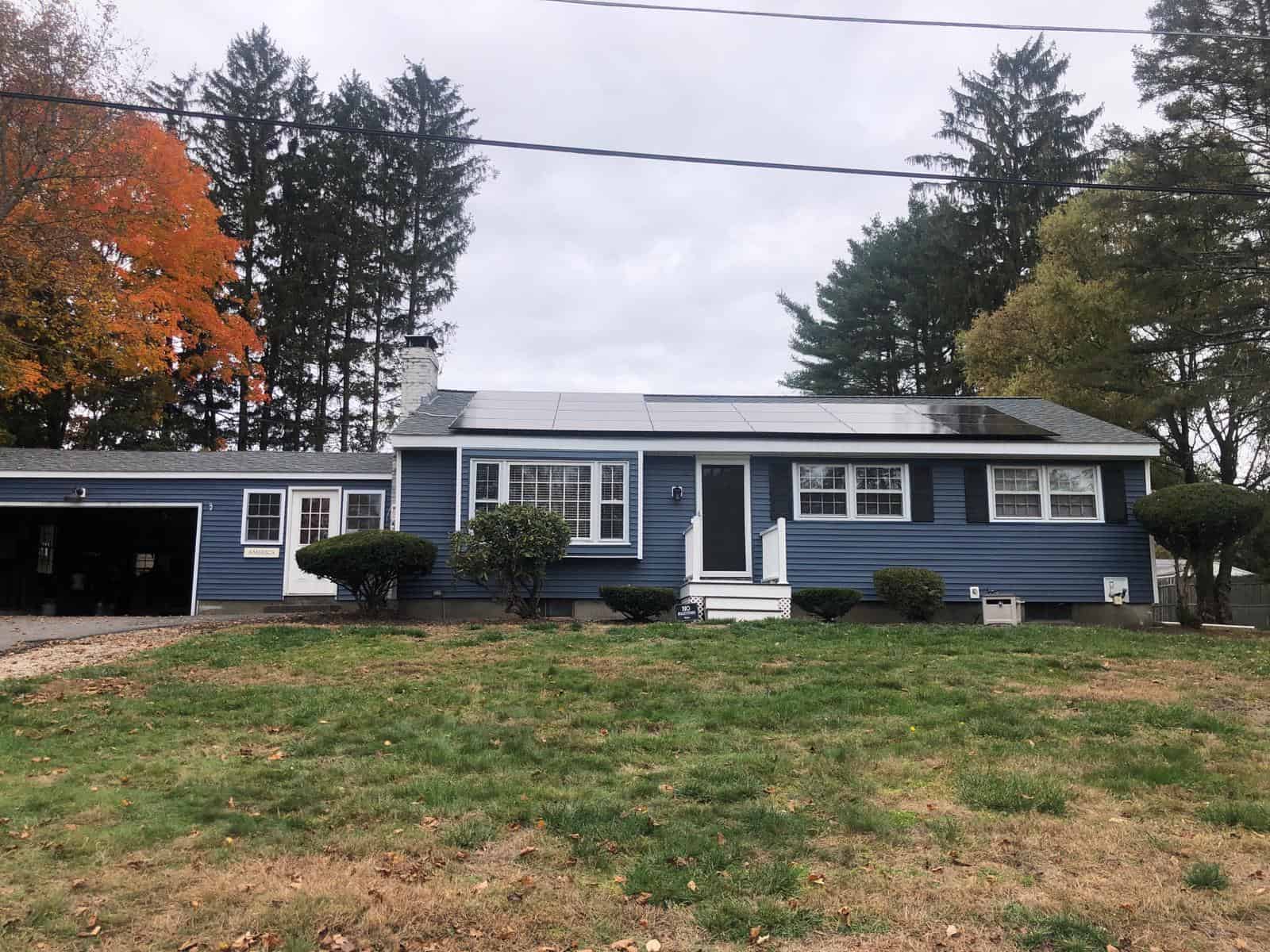 Front view of a blue ranch-style home with rooftop solar panels installed, showcasing residential solar energy, reduced electric bills, and long-term solar savings with a clean, professionally installed solar system.