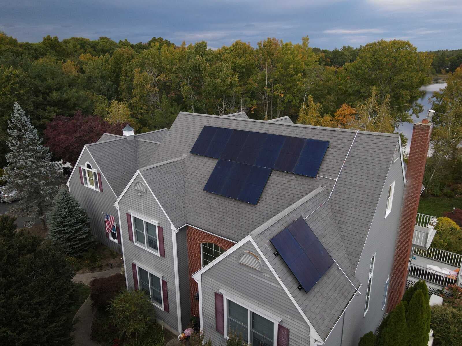 Solar panels installed on the roof of a large suburban house, surrounded by trees with autumn foliage, showcasing residential solar energy system for sustainable power generation.