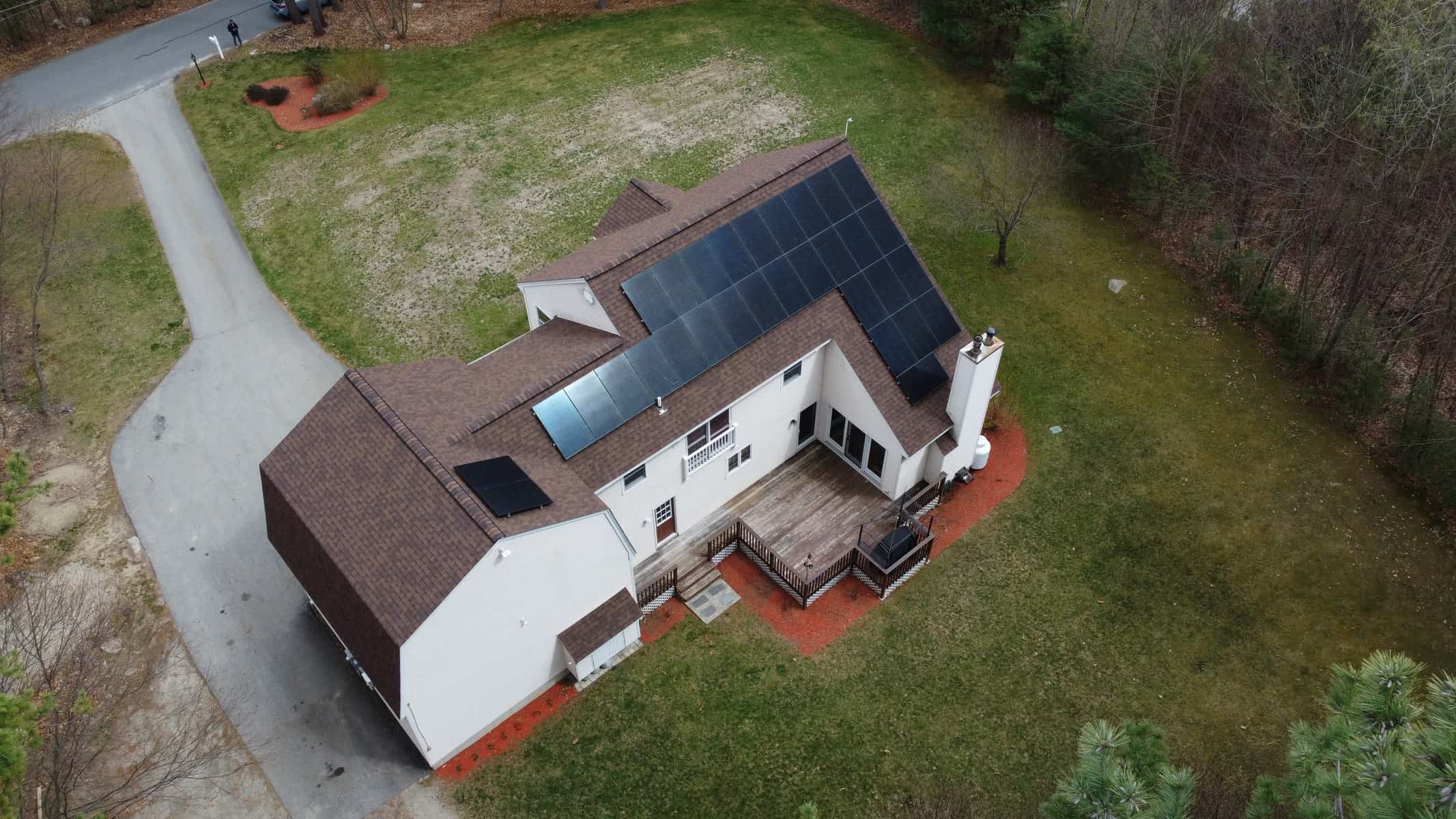 Solar panels installed on the roof of a modern house in a rural area, capturing sunlight for energy, with a backyard deck and surrounding trees, emphasizing sustainable energy solutions for residential homes.
