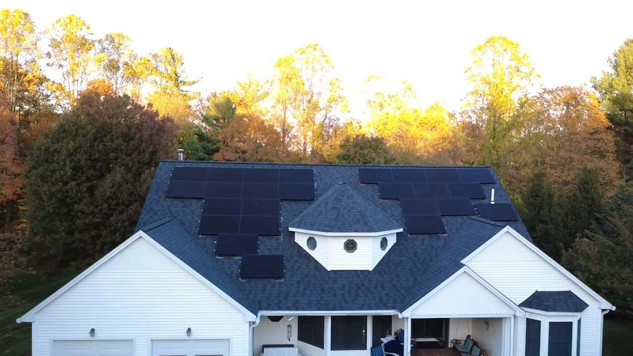 Aerial view of a New England home with black rooftop solar panels installed on an asphalt shingle roof, highlighting residential solar installation, clean energy upgrades, and long-term solar savings for homeowners surrounded by fall foliage.