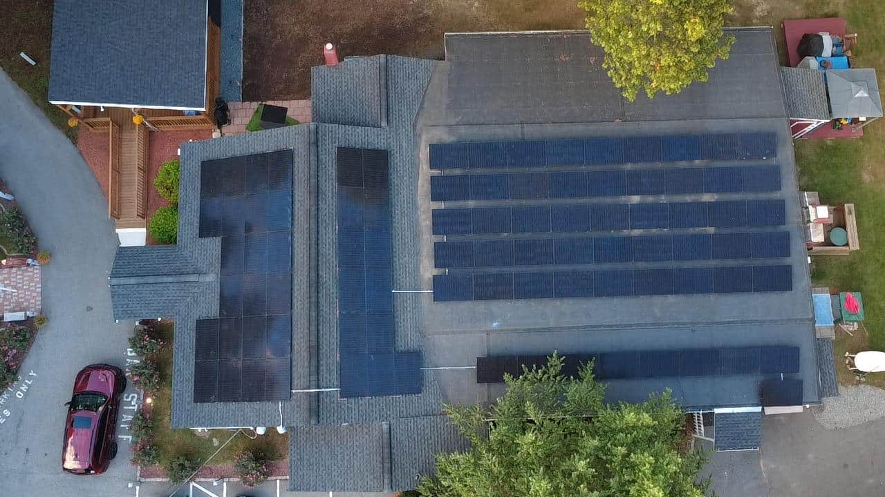 Aerial top-down view of a large residential solar installation featuring multiple roof-mounted solar panel arrays across interconnected asphalt shingle roofs, optimized for maximum solar energy production, long-term solar savings, and reduced electric bills for a New England home using a high-efficiency residential solar system.