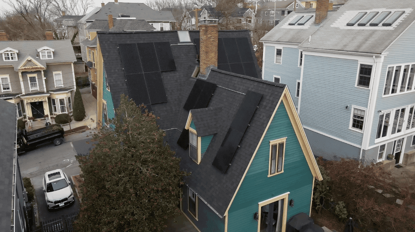 Solar panels on roof of teal residential house, rooftop photovoltaic solar system installed, eco-friendly energy solution, black solar panels with a chimney, surrounded by neighboring homes with blue and yellow exteriors.
