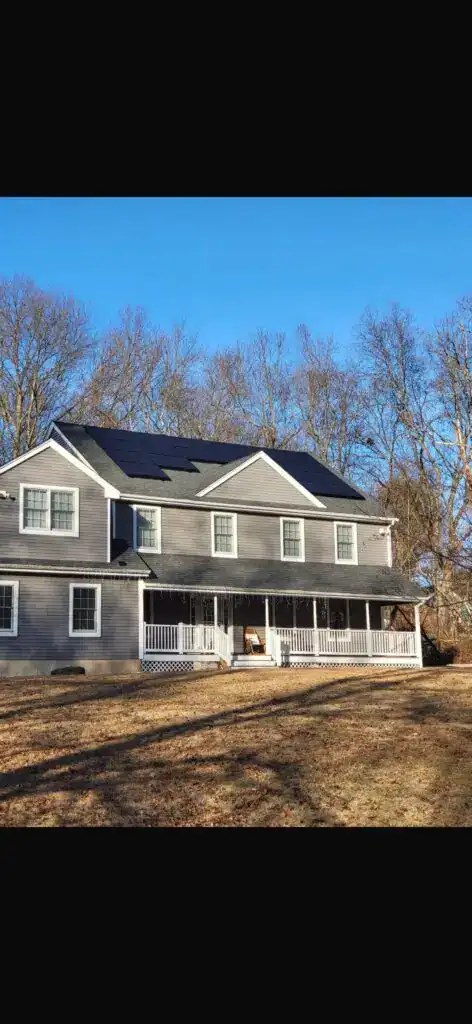 Two-story gray house with a front porch and black solar panels across the roof, generating clean renewable energy.
