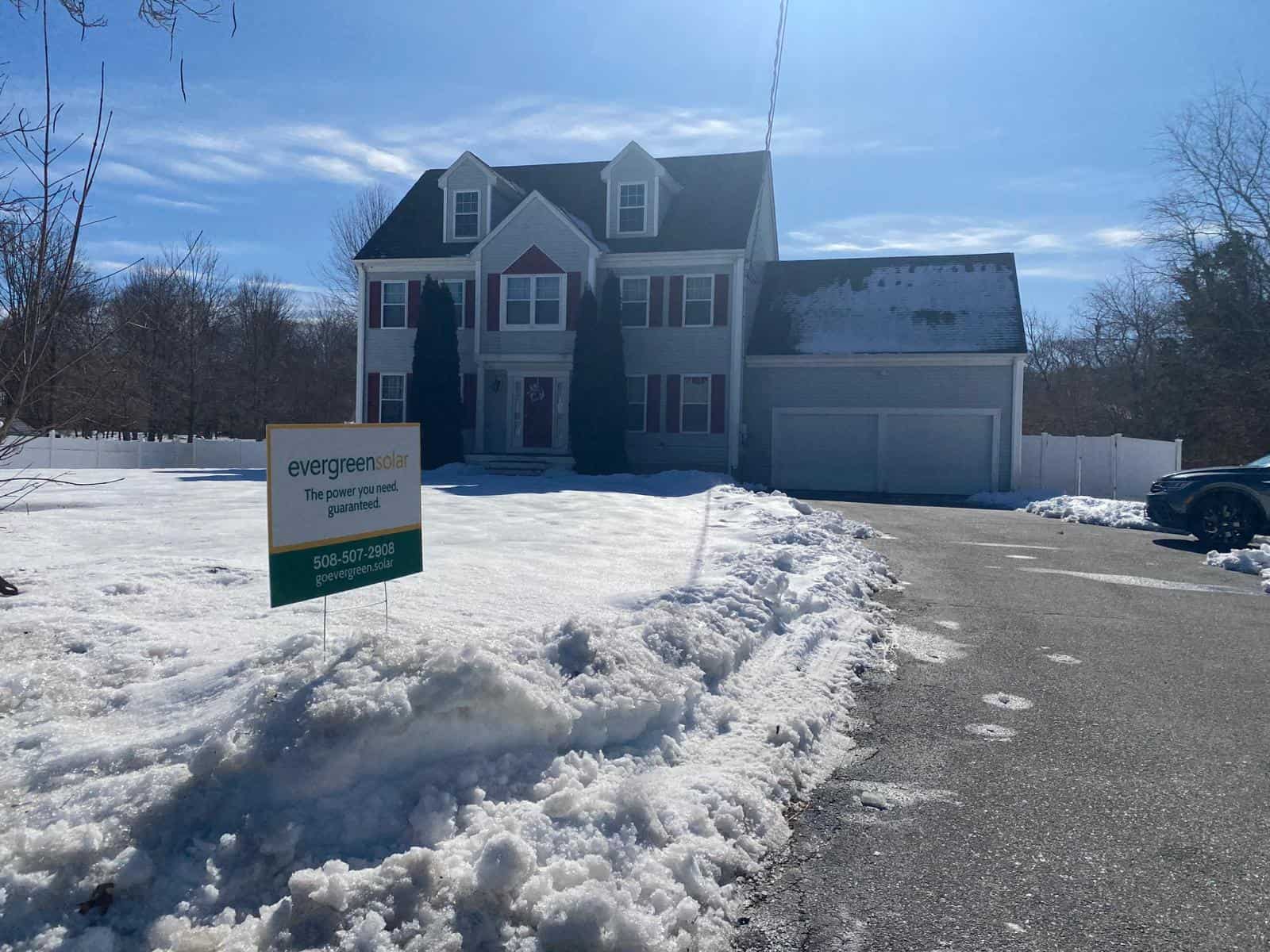 Solar power commercial installation on a suburban home with snow-covered yard and driveway, showcasing Evergreen Solar's environmentally friendly energy solutions.