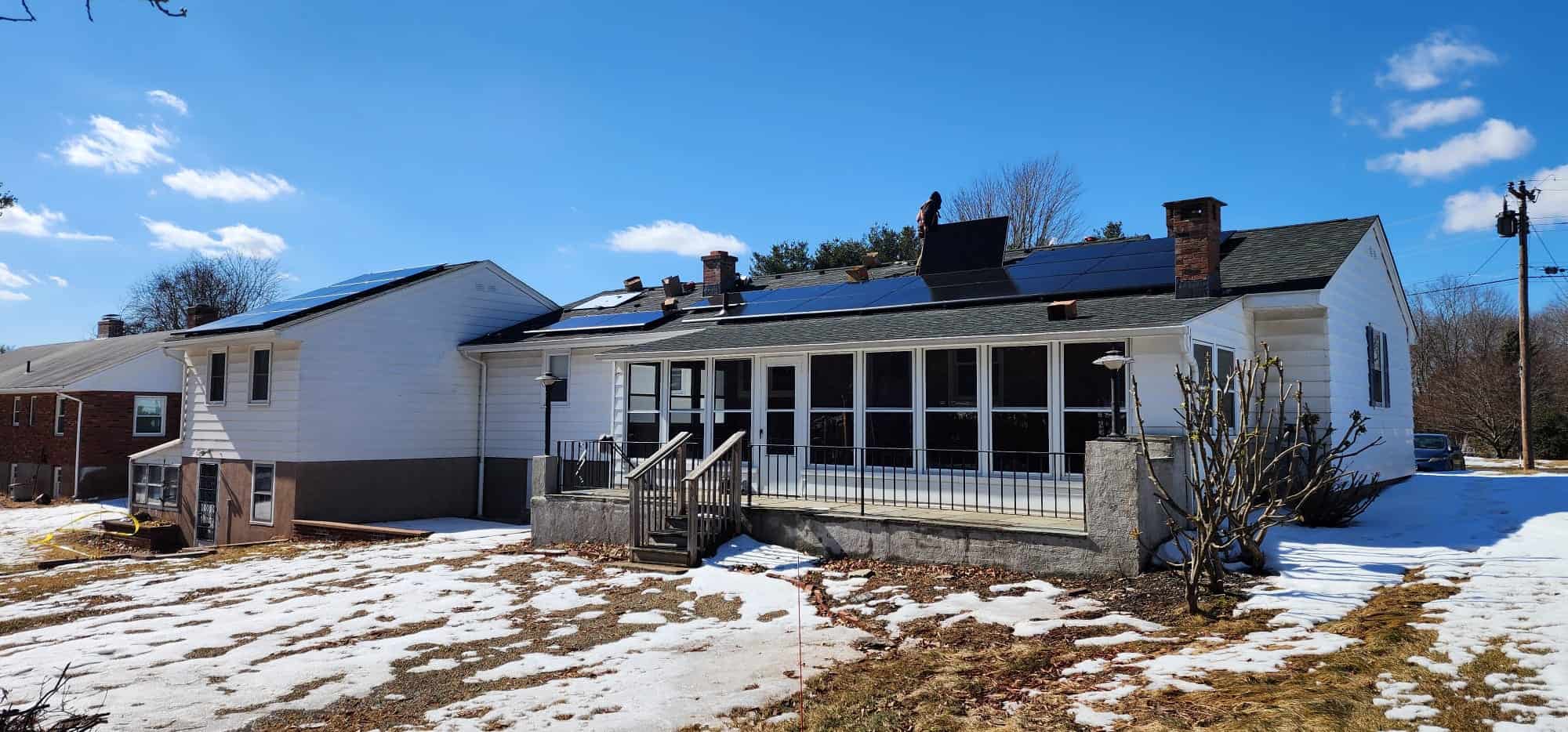 Evergreen Solar panels installed on the roof of a white house with a screened porch, clear blue sky, and snowy yard, showcasing innovative residential solar energy solutions for sustainable living.