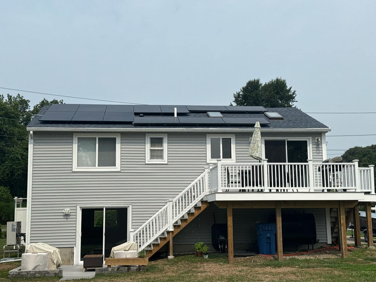 Gray two-story home with a raised deck and black solar panels across the roof, generating renewable energy and reducing electricity bills.