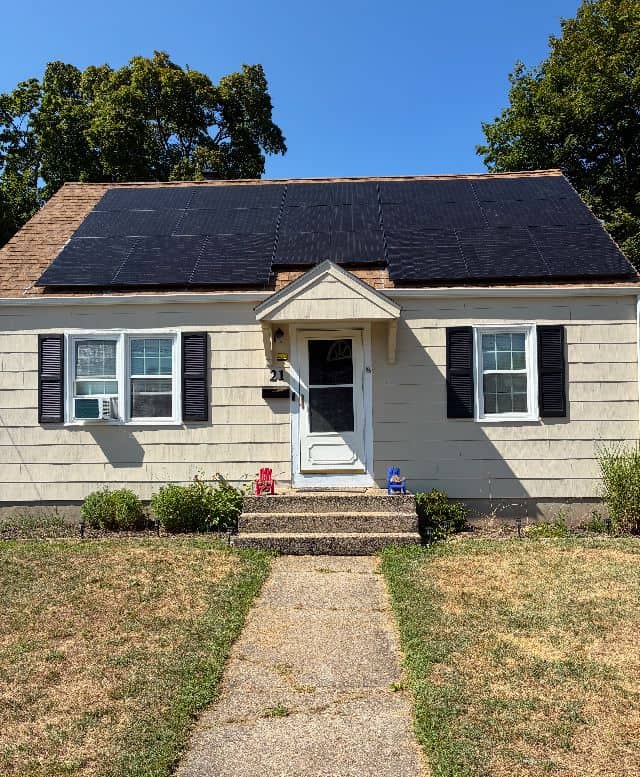 Small beige house with black solar panels covering the roof, providing renewable energy and long-term savings.