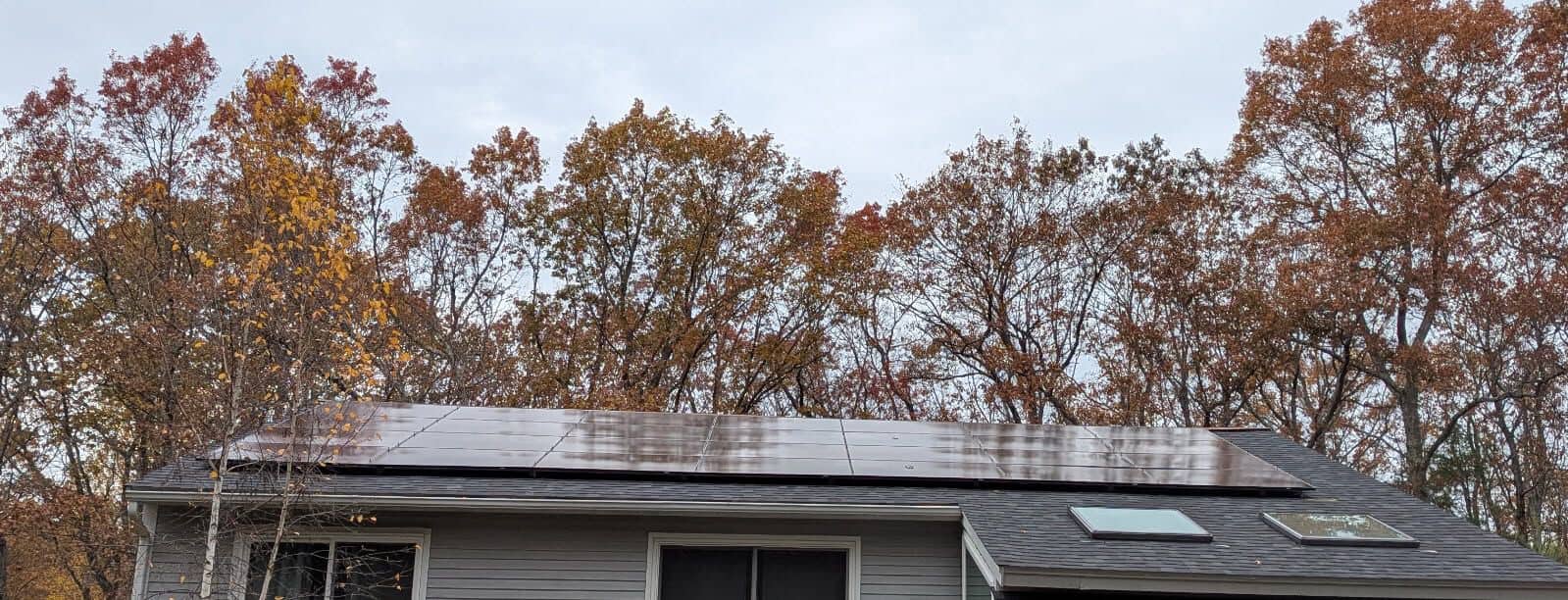 Low-profile rooftop solar panels installed on a New England home, set against fall foliage. The solar array spans the roofline, maximizing energy production while maintaining a clean, streamlined appearance.