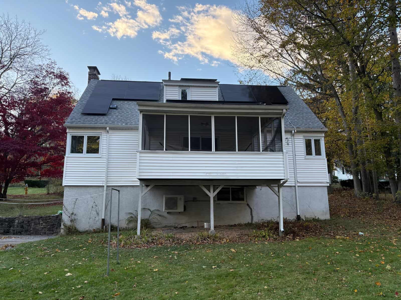 Rear exterior of a New England home featuring a screened-in porch and a cleanly installed solar panel system on the upper roof slopes. The low-profile solar array follows the roofline for a balanced look while supporting efficient residential solar energy production.