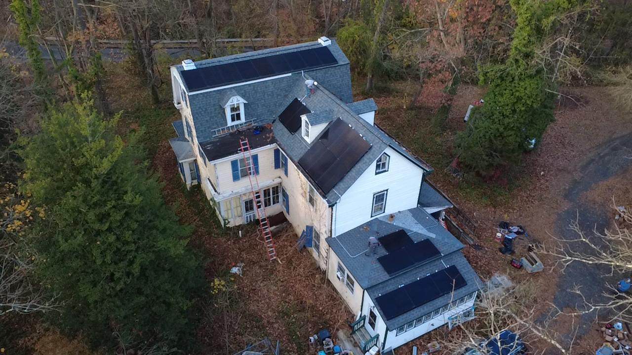Aerial view of a multi-level home surrounded by trees, featuring multiple rooftop solar arrays installed across different roof sections to maximize sun exposure on a complex roof layout.