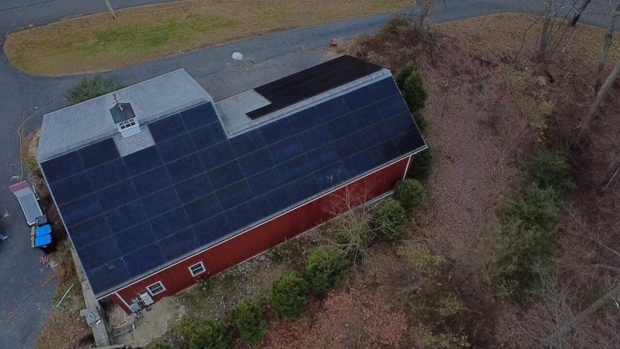 Aerial view of a red barn-style building with a large rooftop solar panel system, designed to maximize solar energy production, increase renewable energy output, and deliver long-term solar savings for a residential property in New England.