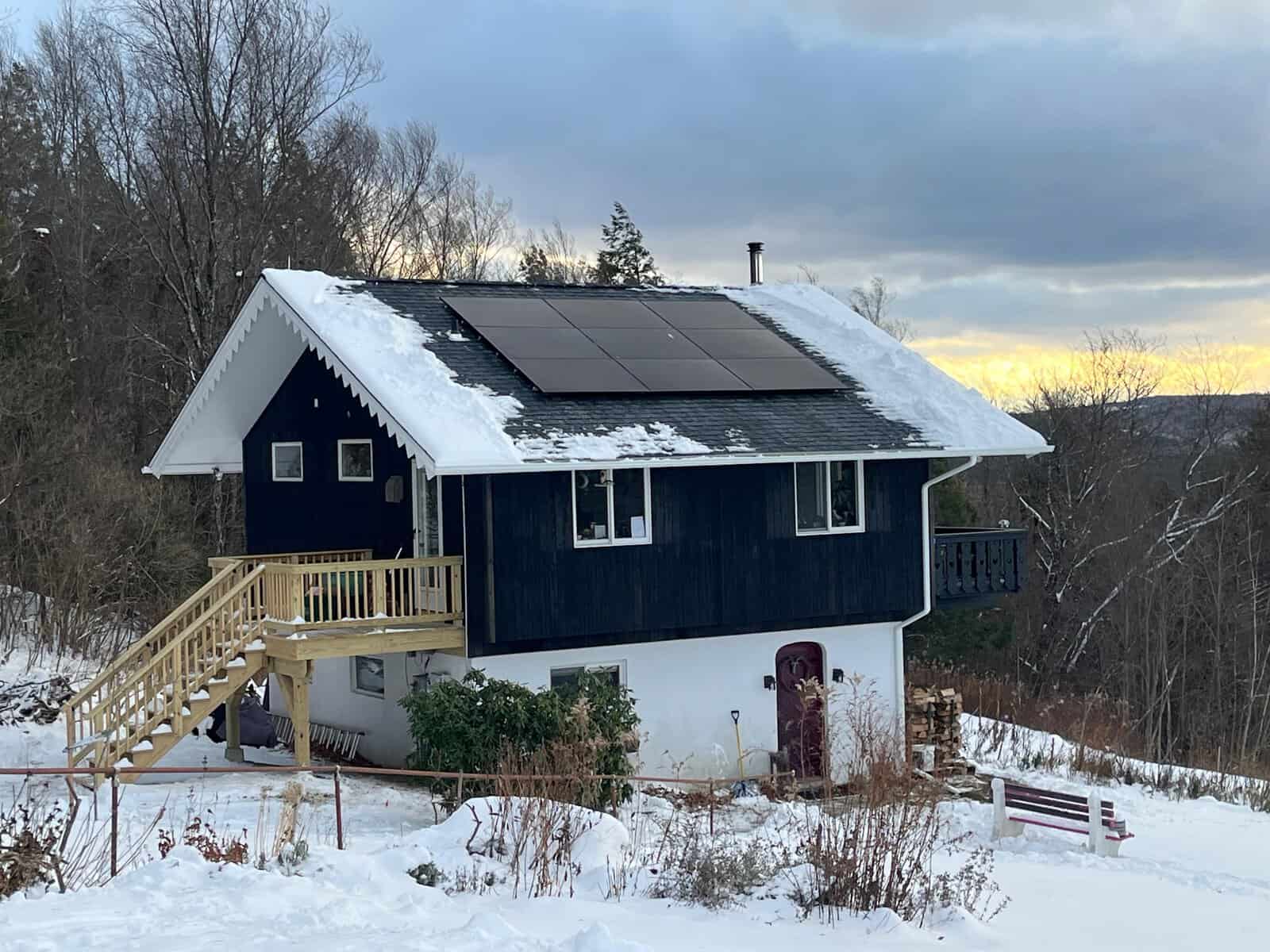 Snow-covered hillside home with a compact solar array installed near the roof ridge, designed to shed snow efficiently while capturing winter sunlight, blending cleanly into a dark exterior typical of New England homes.