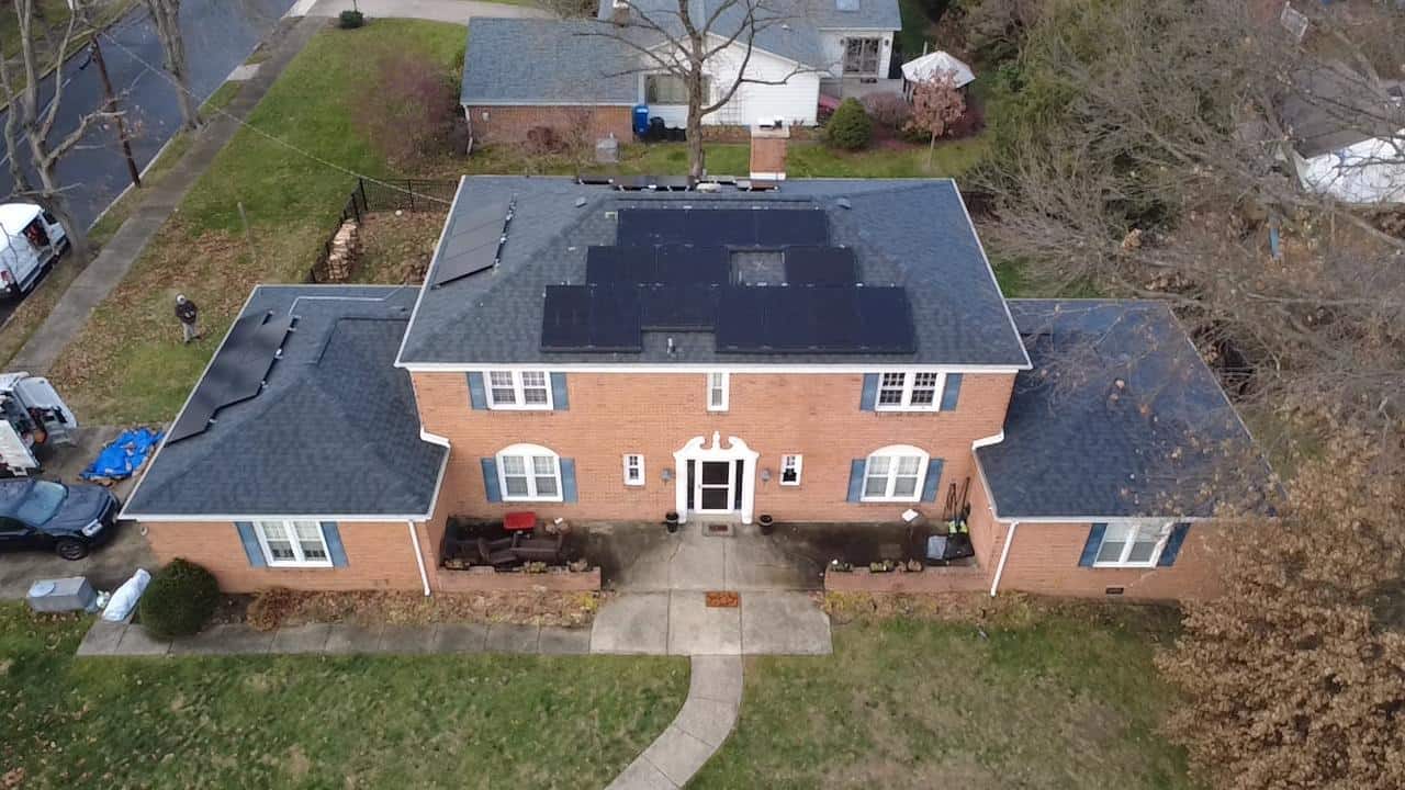Aerial view of a symmetrical brick colonial home with a centrally positioned solar array, cleanly integrated across multiple roof planes to capture sunlight efficiently while preserving the home’s balanced, traditional façade.