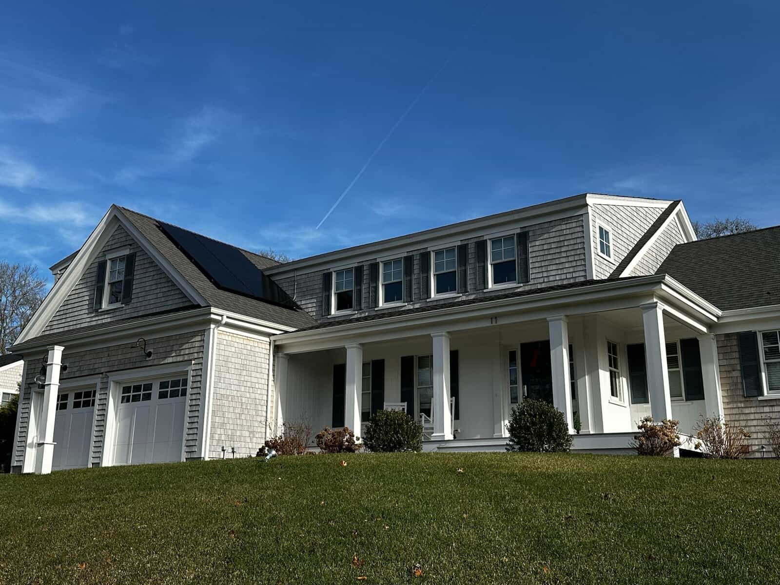 Front exterior view of a New England coastal-style home with cedar shingle siding and a discreet solar panel array integrated into the roof, preserving traditional architecture while delivering efficient, year-round solar energy production.