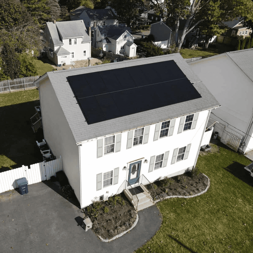 Aerial view of a New England home with fresh solar panels installed across the roof, showcasing a clean, efficient system designed to maximize sunlight and energy savings.